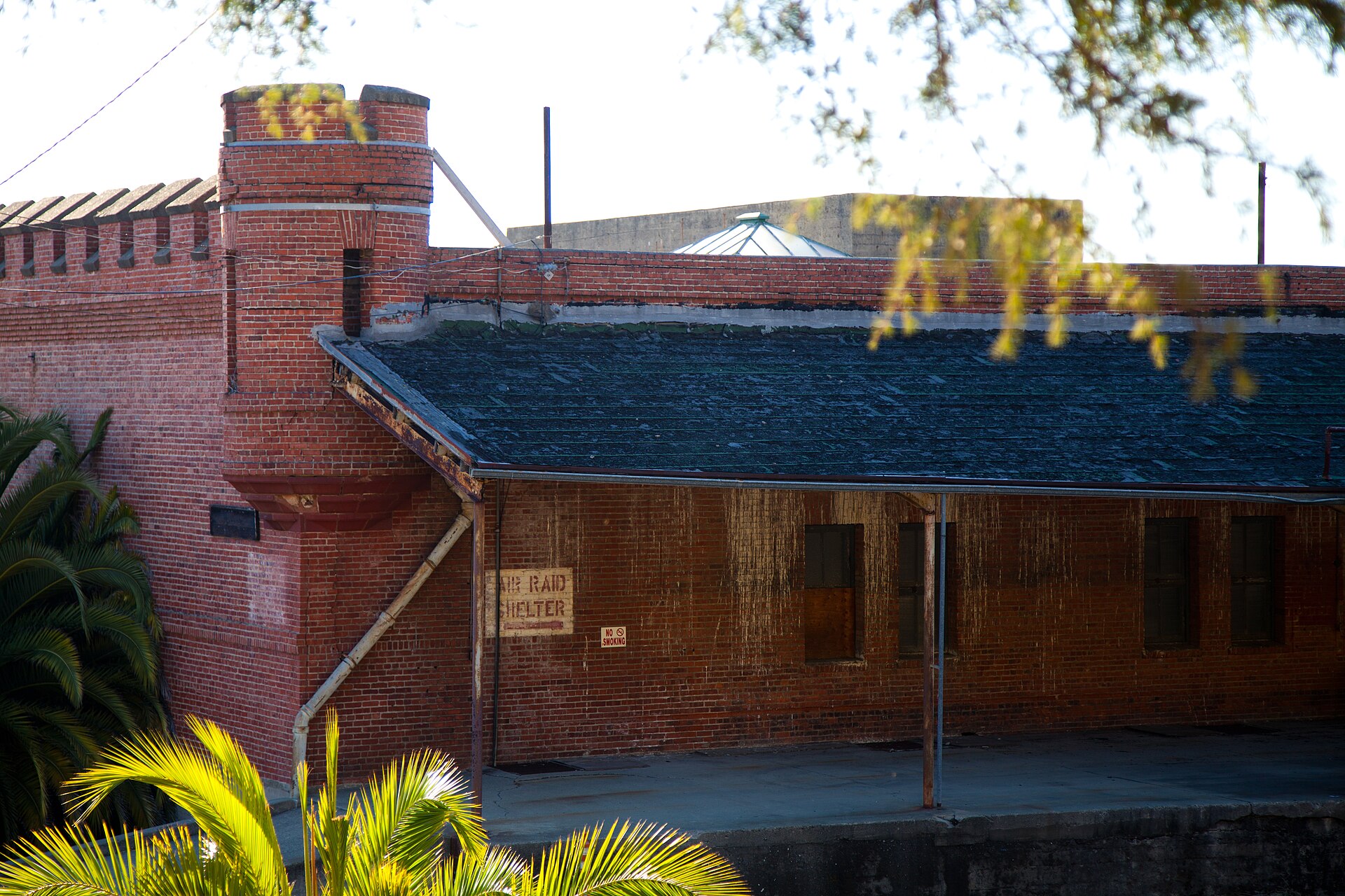 Close view of a brick corner turret, crenellated parapet, and a painted Air Raid Shelter sign from the Navy period
