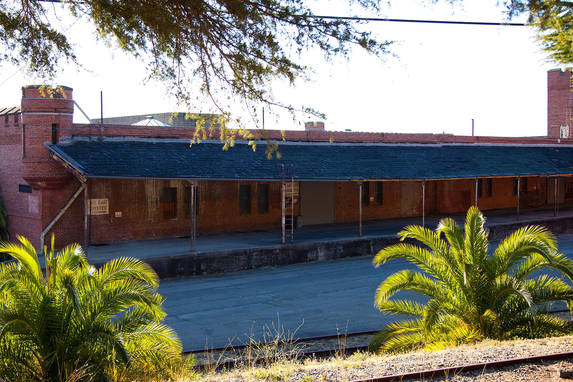 Loading dock along Building 1 with palm trees, rusted railroad tracks, and a Fallout Shelter sign