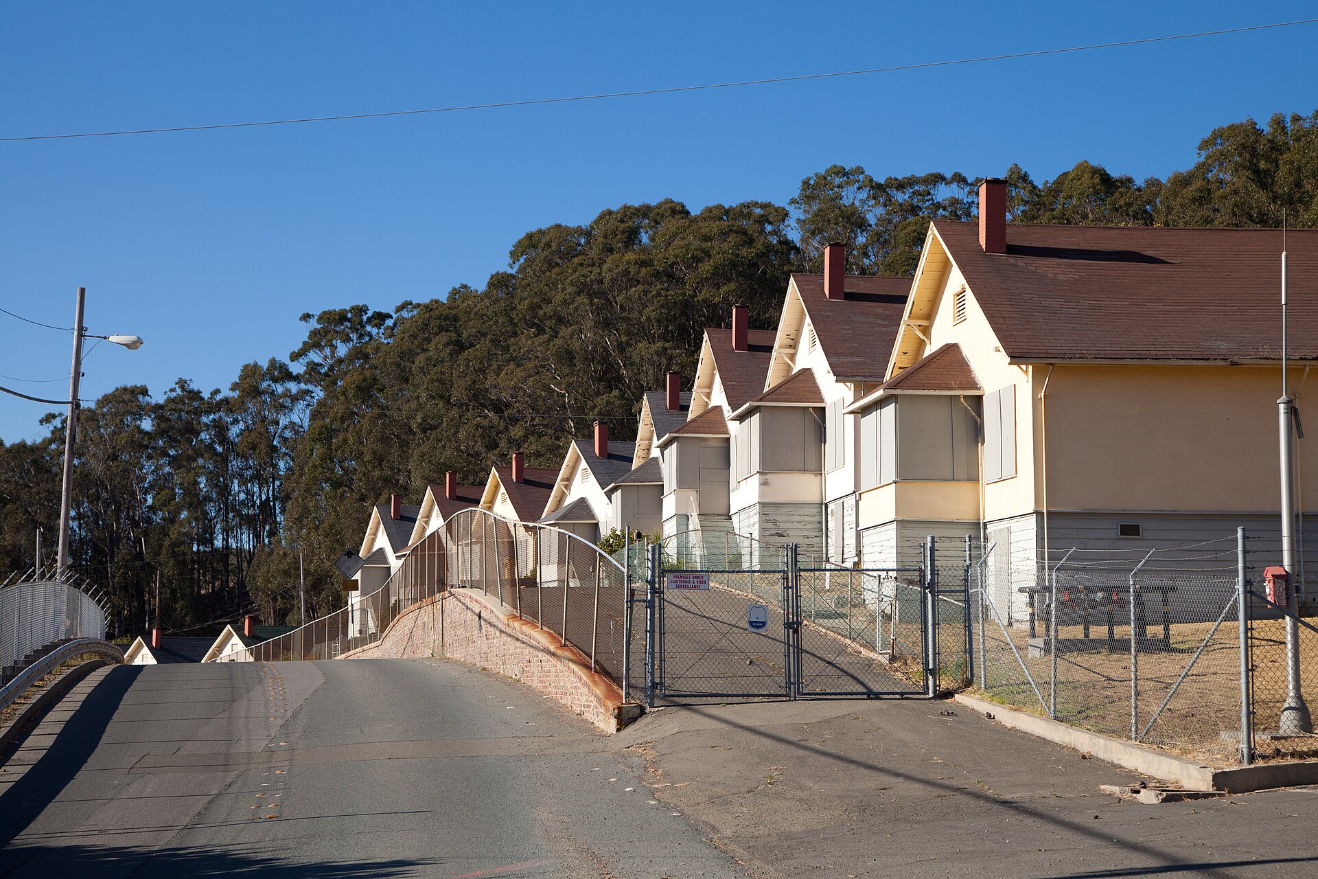 A curving street of nearly identical two-story worker cottages with dark roofs, fenced and boarded